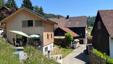 Holzhäuser in ländlicher Umgebung mit Bäumen und klarem Himmel.