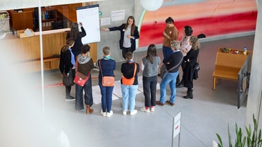 Gruppe von Menschen, die in einem Kreis um ein Whiteboard steht.