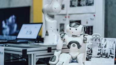 Roboter an einem Tisch mit einem mechanischen Arm im Hintergrund.