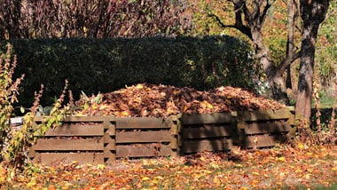 Holzkomposthaufen mit Herbstblättern im Garten.