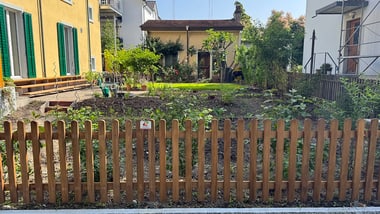 Garten hinter einem Holzzaun, umgeben von Häusern.
