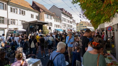 Menschenmenge auf einem Strassenfest mit Bühne und Ständen.