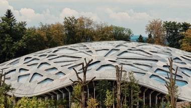 Grosses Gebäude mit markanter Struktur und Bäumen im Hintergrund.