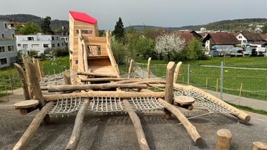 Holzspielplatz mit Kletternetzen und Rutschen in einer Wohngegend.