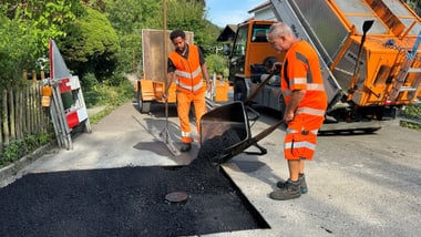 Zwei Personen in orangefarbener Arbeitskleidung reparieren eine Strasse.