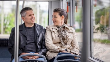 Zwei Personen sitzen lächelnd in einem Bus.