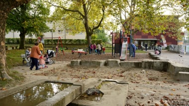 Kinder und Erwachsene in einem Spielplatz mit Spielgeräten und Bäumen.