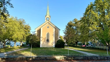Kirche mit Turm umgeben von Bäumen.
