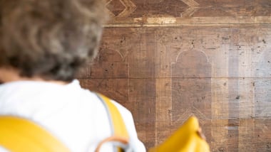 Person in weissem Hemd mit gelbem Rucksack vor historischerHolzwand.