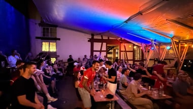 Menschen in einem überdachten Raum mit bunten Lichtern.