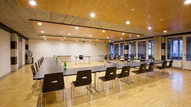 Konferenzraum mit rechteckigem Tischarrangement und leeren Stühlen.