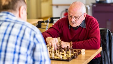 Zwei Personen spielen Schach an einem Tisch.