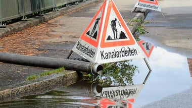 Verkehrszeichen für Kanalarbeiten mit Spiegelung im Wasser.