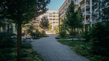 Innenhof mit Bäumen und Wohngebäuden im Hintergrund.