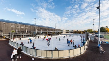 Menschen auf einer Aussen-Eisbahn unter blauem Himmel.
