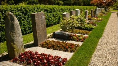 Friedhof mit Grabsteinen und Blumen.