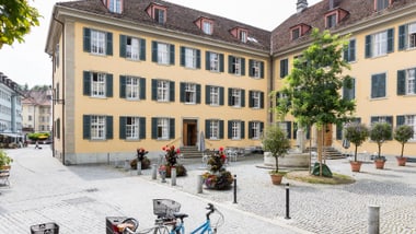 Historisches Gebäude und Fahrräder auf einem gepflasterten Platz.