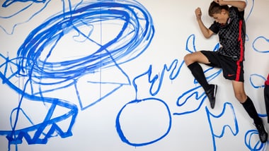 Person in schwarzem Sportoutfit springt vor einer Wand mit blauer Kunst.