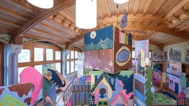 Raum mit Holzdecke und bunter Wandkunst.