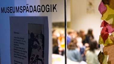 Gruppe von Menschen in einem Raum hinter einem Glas mit der Aufschrift 'Museumspädagogik'.