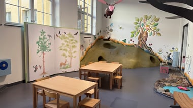 Kindermuseum mit Holztischen, Stühlen und Wandmalereien.
