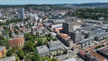 Luftaufnahme einer Stadt mit Gebäuden, Strassen und grünen Flächen.