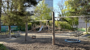 Spielplatz mit Klettergerüst und Bäumen im Hintergrund.