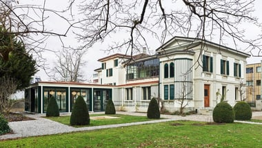 Klassisches Gebäude mit gepflegtem Garten und Bäumen im Winter.