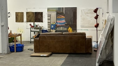 Künstleratelier mit Sofa und Gemälden an den Wänden.