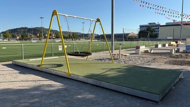 Spielplatz mit Schaukeln und Sportplatz im Hintergrund.