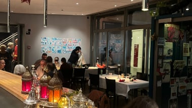 Innenansicht eines Cafés mit sitzenden Gästen und dekorativem Geschirr auf der Theke.