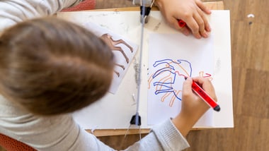 Person zeichnet bunte Linien auf Papier.