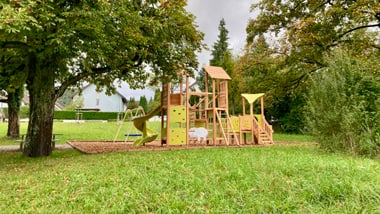 Kinderspielplatz mit Klettergerüst und Rutsche, umgeben von Bäumen.