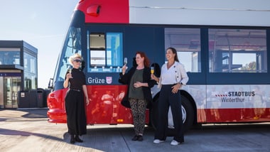 Drei Personen stehen vor einem roten Bus und halten Eiscreme.