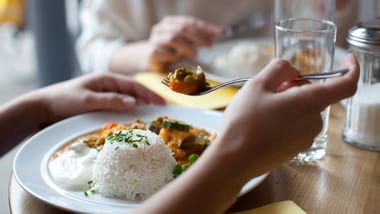Personen essen an einem Tisch Reisgericht mit Gemüse.