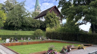 Grüne Rasenfläche mit Blumenarrangements, Kirche und Gebäude im Hintergrund.