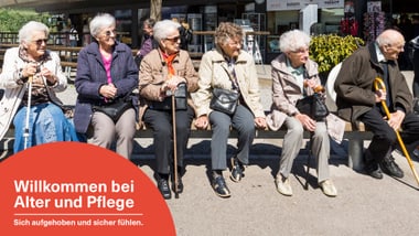 Sechs ältere Personen sitzen auf einer Bank im Freien.