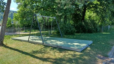Leerer Spielplatz mit Schaukel auf Grasfläche.