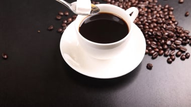 Tasse Kaffee mit Zuckerwürfel auf einem Löffel und Kaffeebohnen.