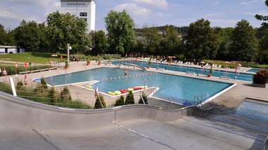 Freibad mit Wasserrutsche und Pool unter blauem Himmel.