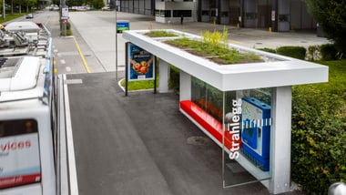 Bushaltestelle mit Werbeplakat, neben der ein Bus steht.