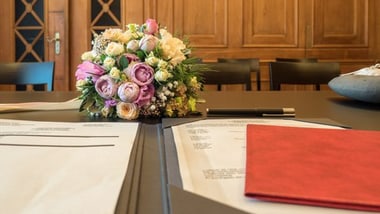EinEin Ausschnitt des Trauzimmers mit einem Blumenstrauss auf einem Tisch mit Dokumenten in holzvertäfeltem Raum.