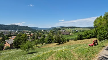 Landschaftsblick mit Häusern und Hügeln unter blauem Himmel.
