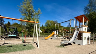 Spielplatz mit Schaukeln und Rutschen bei sonnigem Wetter.