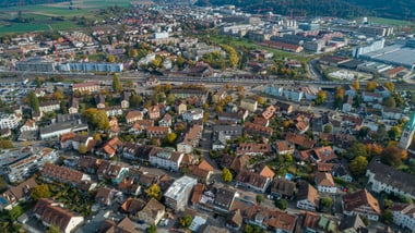 Luftaufnahme einer Stadt mit Häusern, Strassen und grünen Feldern im Hintergrund.