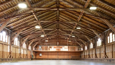 Innenansicht einer grossen Holzhallenkonstruktion mit sichtbarem Dachgebälk.
