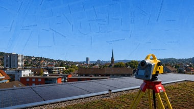 Vermessungsgerät auf einem Dach mit Solarzellen, Stadt im Hintergrund.