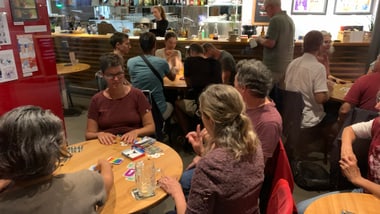 Gruppe von Menschen in einem Café, die Karten spielen.