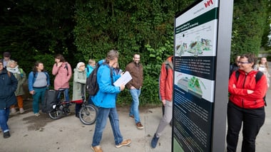 Gruppe von Menschen spaziert neben einem Schild im Freien.