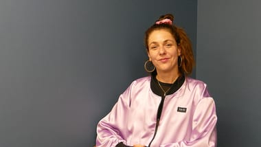 Person mit rosa Jacke vor blauer Wand.